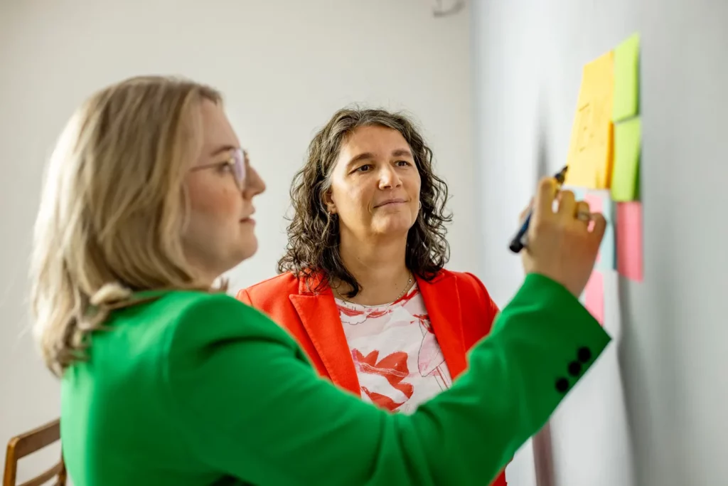 Dominique Woith und Katja Beckmeyer arbeiten an einer Wand mit Haftnotizen