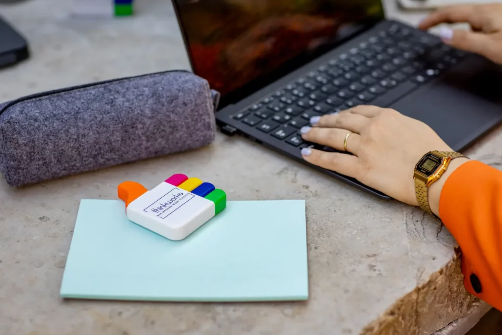 Hände tippen auf einem Laptop, daneben ein thinkworks-Textmarker auf einem Notizblock